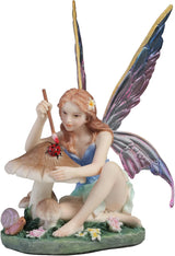 Fairy figurine with colorful wings sitting on a mushroom painting a ladybug.
