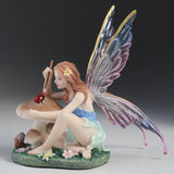 Fairy figurine with colorful wings sitting near a mushroom painting a ladybug.