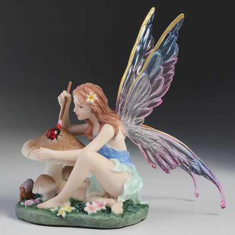 Fairy figurine with colorful wings sitting near a mushroom painting a ladybug.