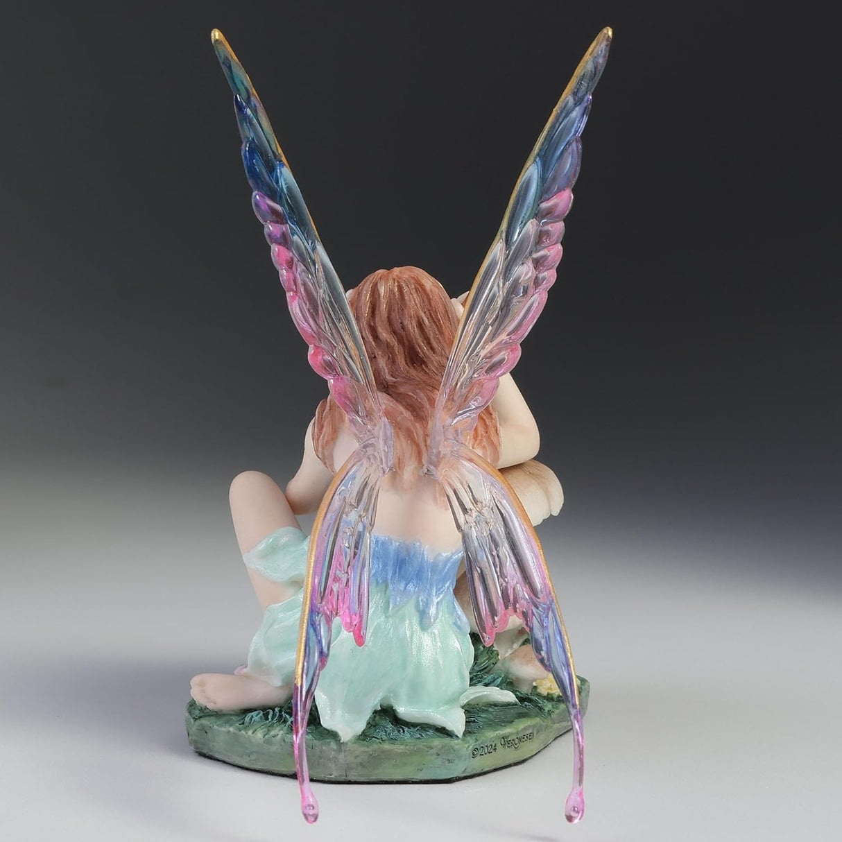 Fairy figurine with colorful wings sitting near a mushroom painting a ladybug.