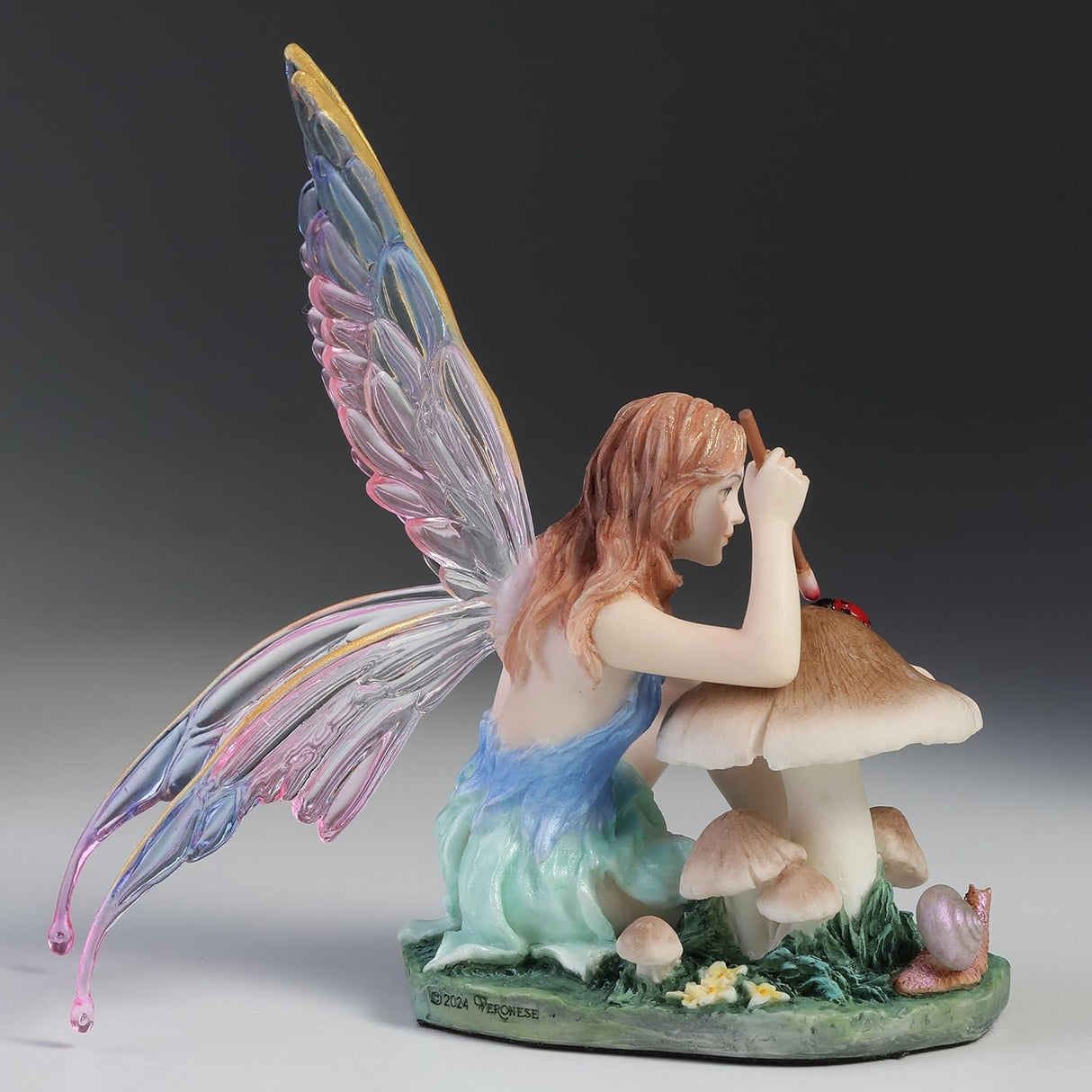 Fairy figurine with colorful wings sitting near a mushroom painting a ladybug.