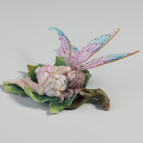 Fairy figurine with colorful wings, cuddling a bunny on a leaf