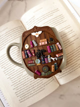 Decorative bookshelf mug with miniature books and items shown on an open book