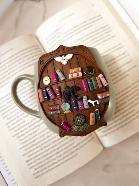 Decorative bookshelf mug with miniature books and items shown on an open book