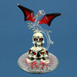 Glass figurine featuring red and black winged dragon with gold accents on stack of three red-eyed skulls on mirrored base