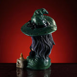 Figurine of witch in green hat, striped purple and black stockings, purple hair holding black cat, next to skull candle, shown from the back