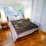 Woven blanket with a design of cats and books with trinkets on a bookshelf. Shown on a bed