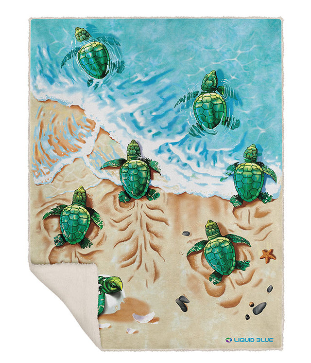 A rectangular throw blanket featuring an illustrated beach scene with green sea turtles swimming in turquoise water and walking on sandy beige shore. The blanket is shown laid flat against a white background, with one corner folded over to reveal a cream underside.