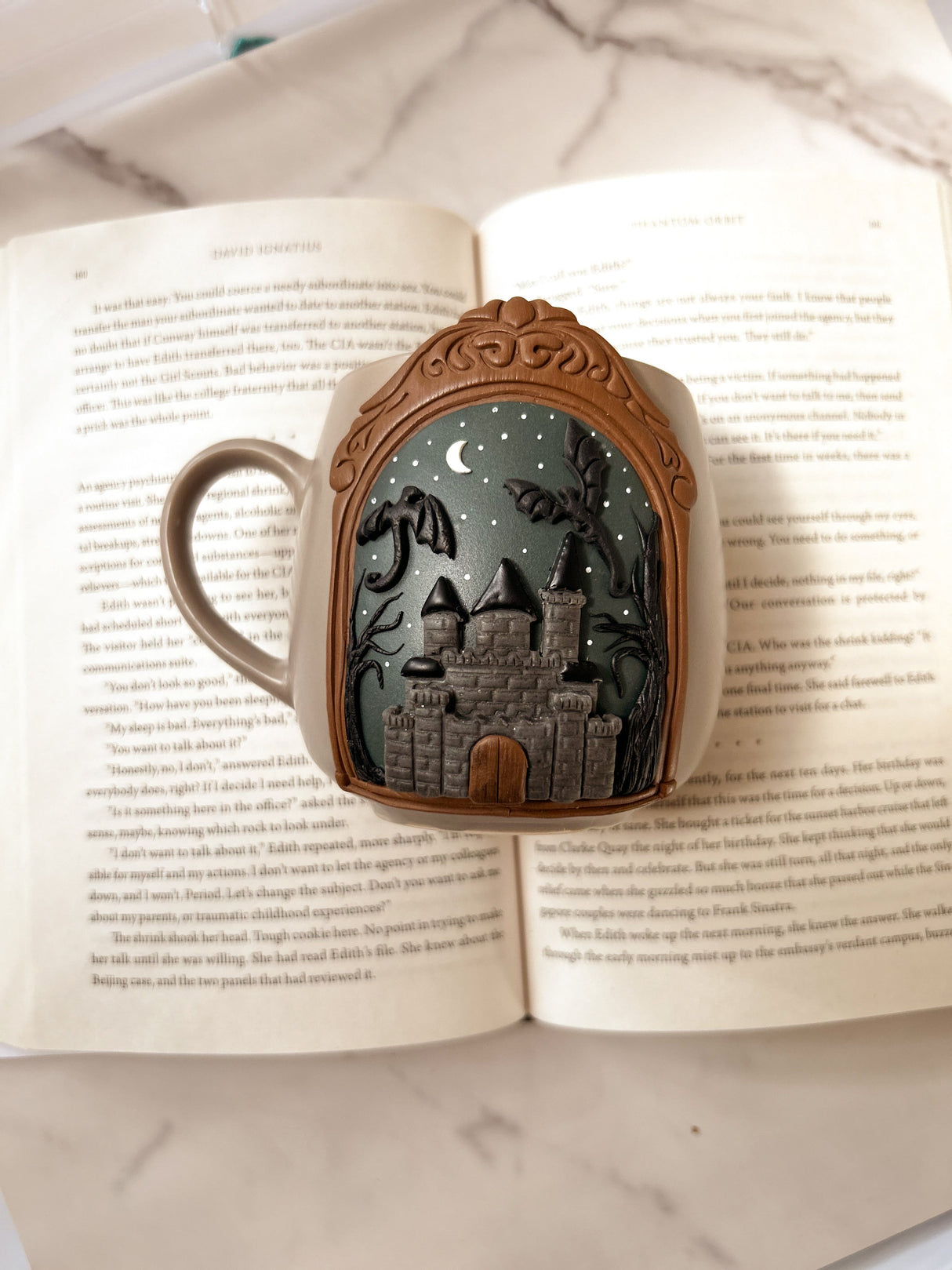 Decorative mug with a castle and dragon design in clay, displayed on an open book
