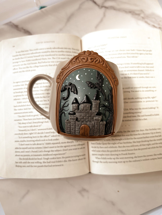 Decorative mug with a castle and dragon design in clay, displayed on an open book