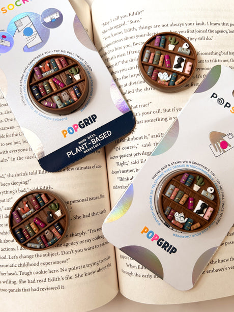Two miniature bookshelves popsocket phone grips, shown on an open book