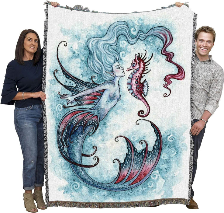 Tapestry blanket by Amy Brown showing mermaid in shades of blue with pink accents, and pink seahorse. Shown held by two adults