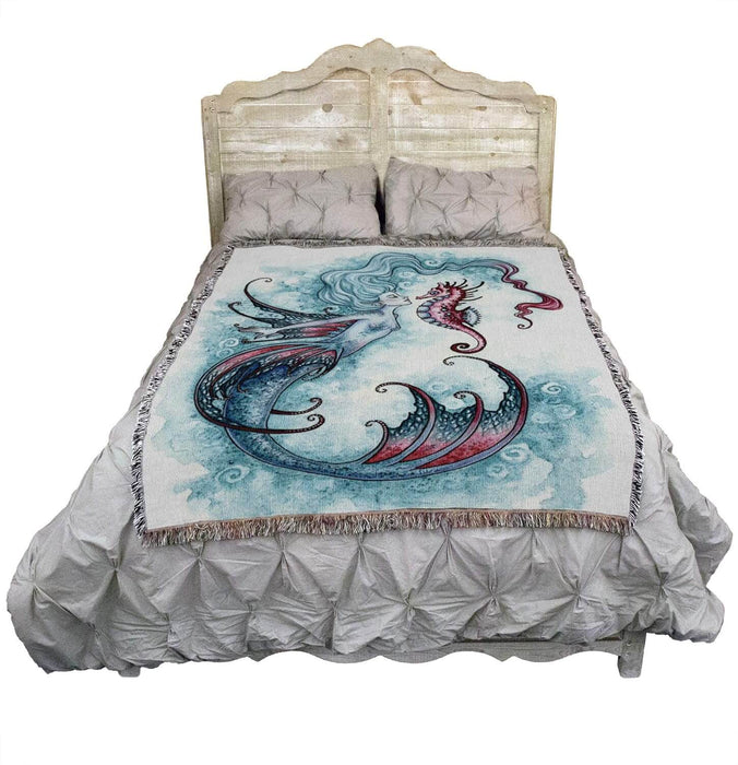 Tapestry blanket by Amy Brown showing mermaid in shades of blue with pink accents, and pink seahorse. Shown on a bed