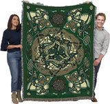 Tapestry blanket in green, gold and cream with Celtic hound knotwork design, held up by two people to show large size