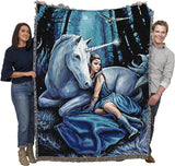 Tapestry blanket of a woman in blue dress and unicorn with glowing horn in a moonlit forest at night. Shown held by two adults