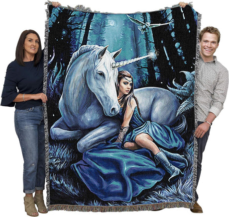 Tapestry blanket of a woman in blue dress and unicorn with glowing horn in a moonlit forest at night. Shown held by two adults