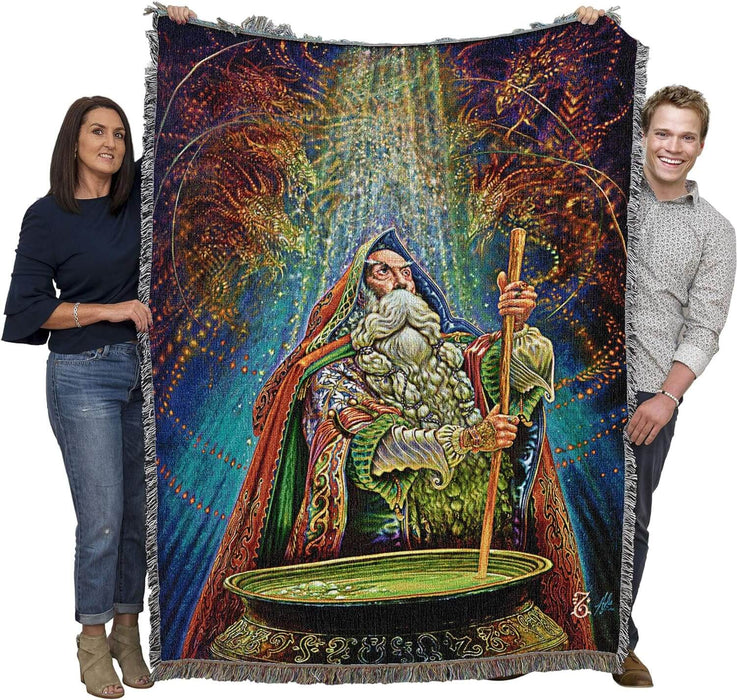 Tapestry blanket with art by Myles Pinkney. Wizard stirring a cauldron with magical dragons in the air above. Shown held by two adults