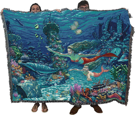 Blanket with mermaid design held by two people, featuring underwater scene with mermaids and fish.