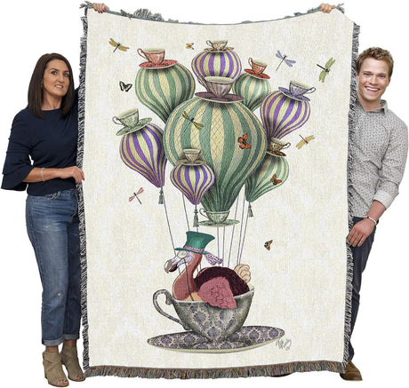 Woven blanket with a colorful design of a dodo in a teacup on hair balloon with dragonflies and butterflies, held up by two adults