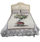 Woven blanket with a colorful design of a dodo in a teacup on hair balloon with dragonflies and butterflies, shown on a bed