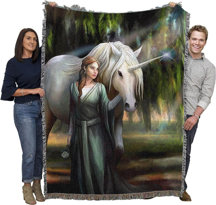 Tapestry blanket with art by Anne Stokes featuring a woman in green with a unicorn standing amidst mossy trees. Shown held by two adults