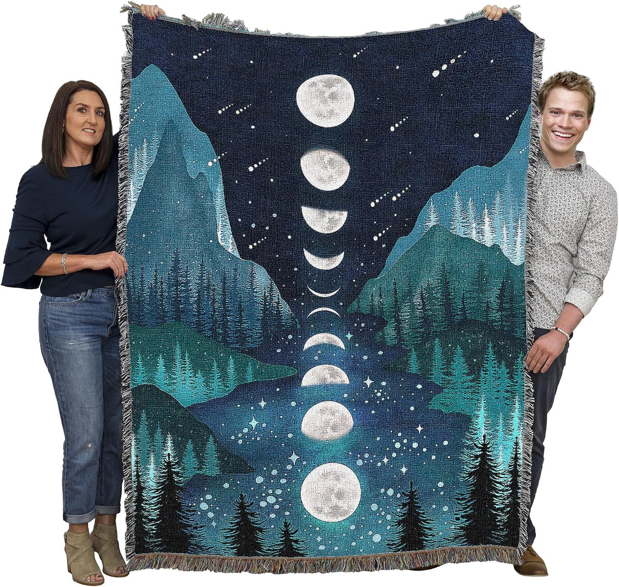 Two people holding a large blanket with a moon phase design over a mountain and forest landscape.