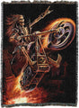 Skeletal figure on a motorcycle with flames and gravestone in the background on a woven blanket.