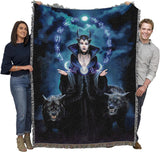 Two people holding a large blanket with a fantasy design of a witch and wolves.