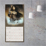 Calendar example for May with a fantasy-themed cover featuring a woman with long hair and armor, displayed on a textured wall.