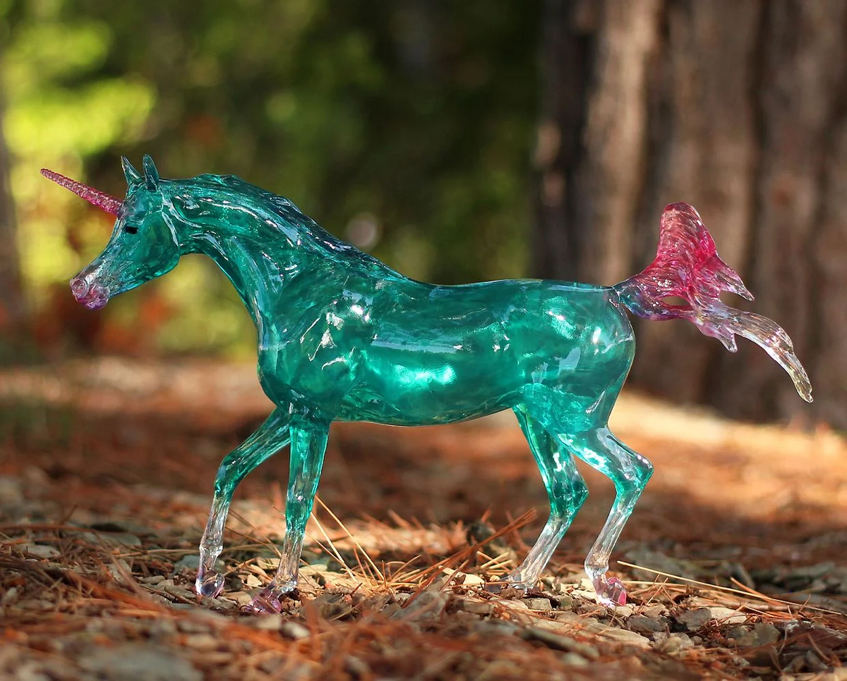 Model unicorn with clearware aqua body, white socks and tail tip, pink hooves, tail, mane, nose and horn, shown in the forest