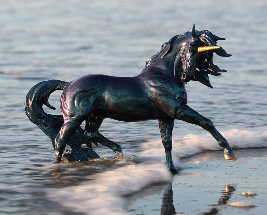Iridescent black-blue-purple unicorn figurine on a beach