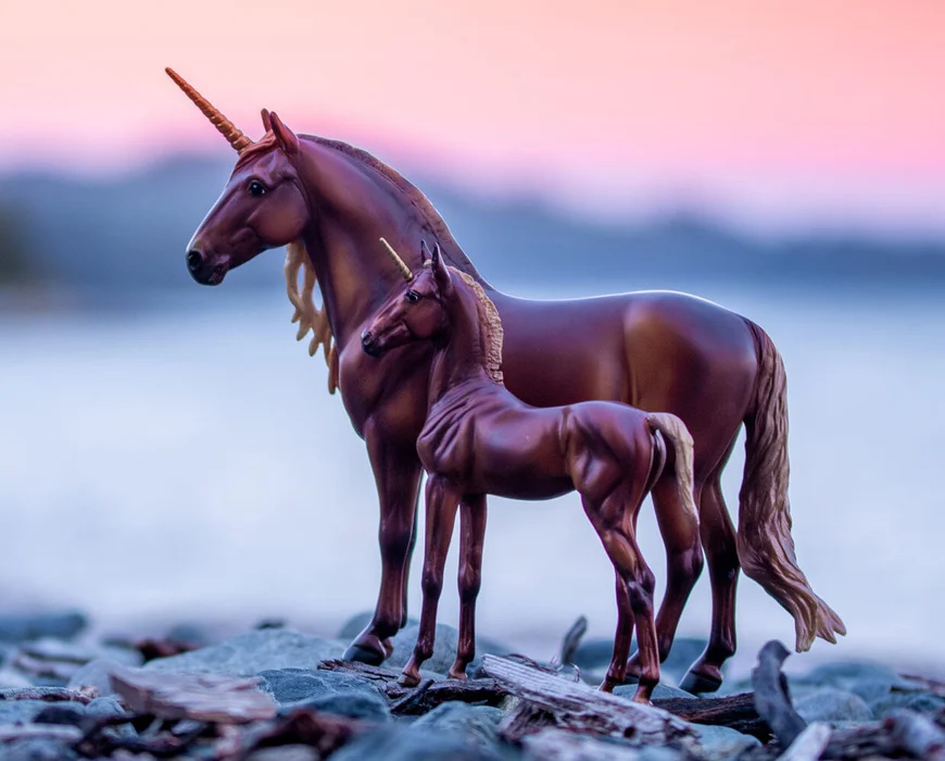Unicorn and horse figurines standing on a beach with a sunset in the background