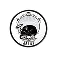 White coaster with black cat with halo sleeping on skulls above word "Saint"