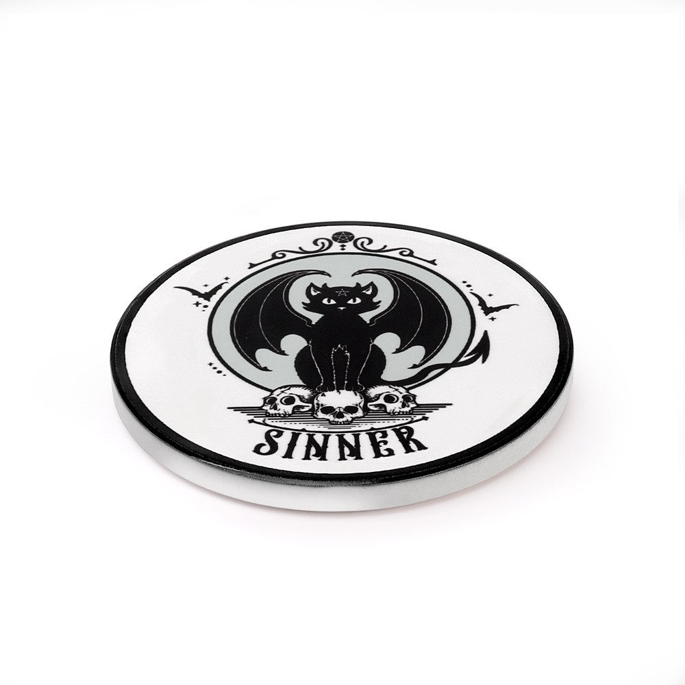 Ceramic coaster, white with black winged cat sitting on skulls with word "Sinner" underneath