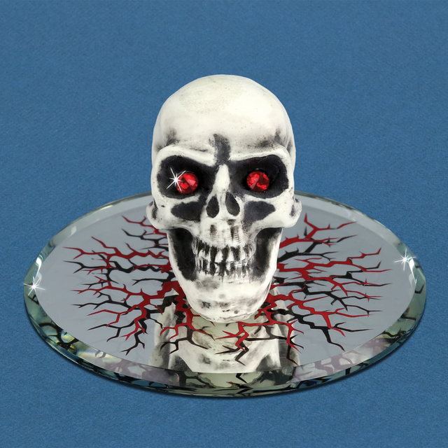 Glass skull figurine with red crystal eyes on a decorated mirrored base