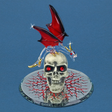 Glass figurine of dragon with red and black wings and gold accents on a white skull with red eyes, on a mirrored base