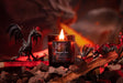 Candle labeled 'Dragon Fire' with a dragon figurine and smoldering embers in a dark setting.