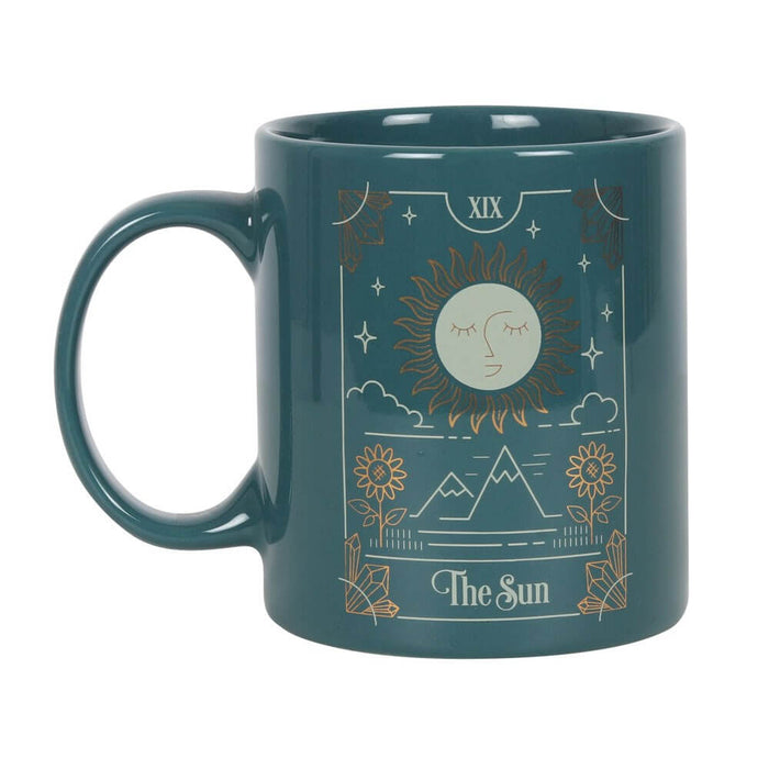Rich green coffee mug with white and gold foil design for The Sun tarot card with an eyes closed sun above mountains.