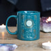 The Sun tarot mug shown on a table with out of focus crystals and candles