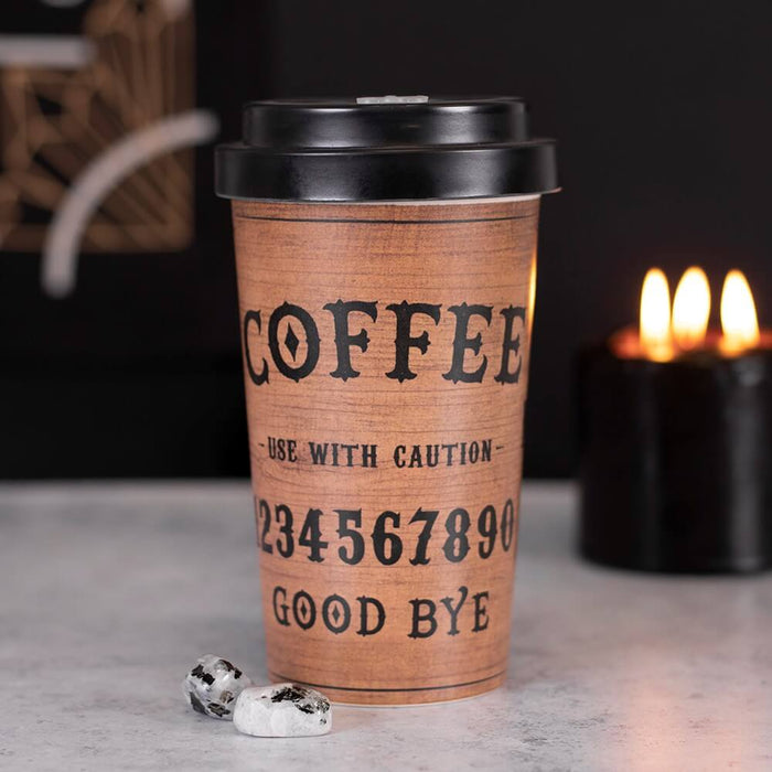 Coffee 'talking board' travel mug with black lid shown with out of focus candle