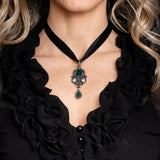 Ornate pewter necklace with green and clear gemstones, skull accent, Gothic style, shown worn on ribbon