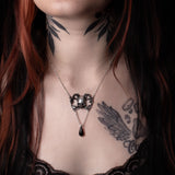 Close-up of a person with tattoos wearing a necklace with a skull pendant.