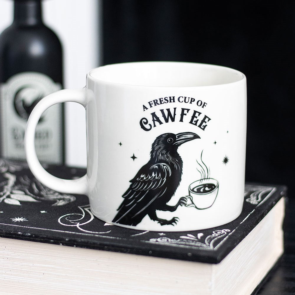 White mug with a black crow design and text sitting on a book