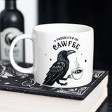 White mug with a black crow design and text sitting on a book