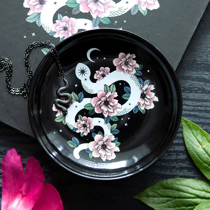 Trinket dish showing white snake with crescent moon, pink flowers on black ceramic background. Shown with a necklace for example