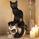 Figurine of black cat sitting on skull adorned with black roses