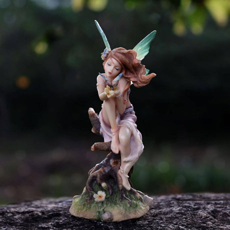 Figurine of a fairy leaning towards the butterfly on her hands. Red hair, green tipped wings, pink dress, sitting on a tree stump.