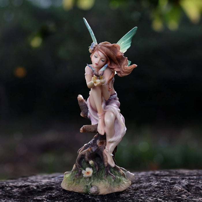 Figurine of a fairy leaning towards the butterfly on her hands. Red hair, green tipped wings, pink dress, sitting on a tree stump.
