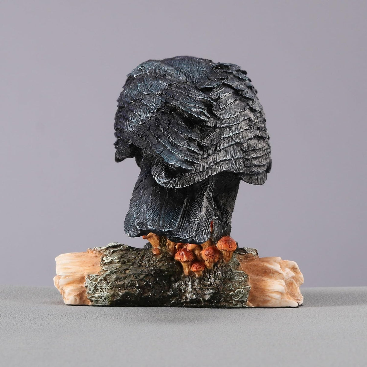 Black crow figurine on a log, shown from the back