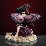 Fairy figurine of pixie with purple and black wings and outfit holding a dragon staff and sitting on skulls. Shown from the back